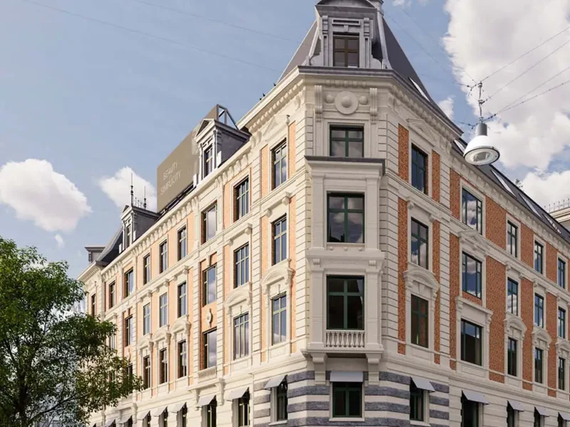 Historisches Eckgebäude mit Stuckfassade, roten Ziegelbändern und Granitsockel, davor Cafébestuhlung