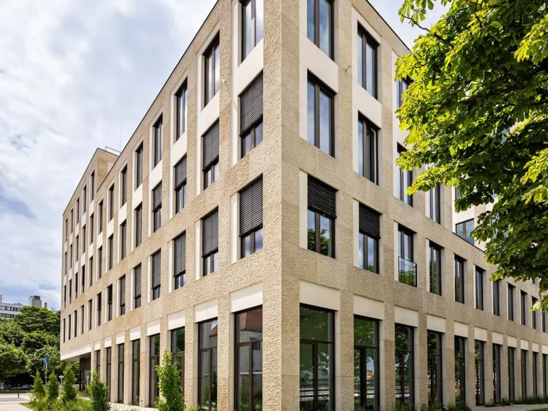 Bürogebäude mit heller Natursteinfassade und tiefen Fensterlaibungen, umgeben von Grünflächen