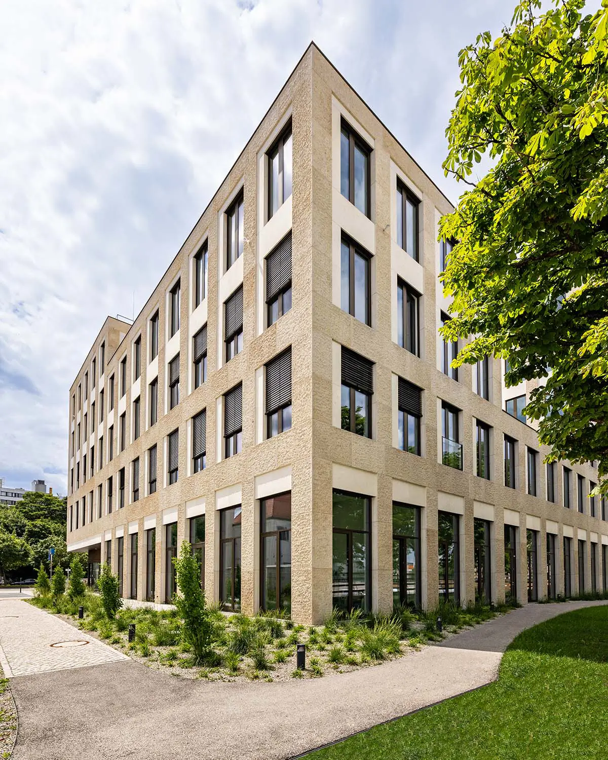 Bürogebäude mit heller Natursteinfassade und tiefen Fensterlaibungen, umgeben von Grünflächen
