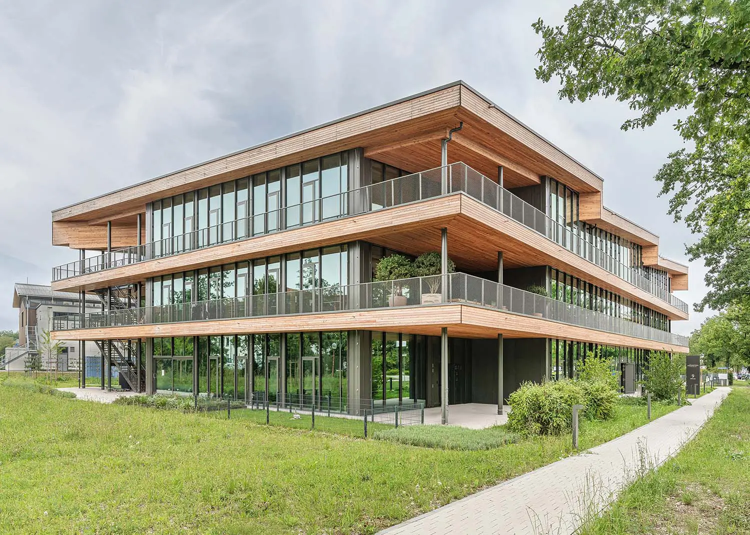 Dreigeschossiges Bürogebäude in Holzbauweise mit auskragenden Geschossdecken, umlaufenden Balkonen und Glasfassade, davor eine Wiese