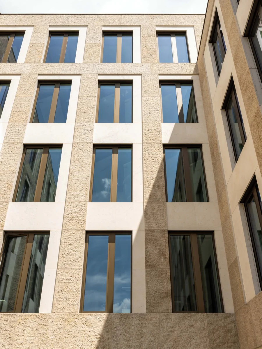 Untersicht einer Bürofassade aus hellem, gestocktem Naturstein mit hohen schmalen Fenstern in Bronzerahmen
